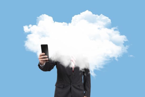 Businessman with his head in the clouds consulting with the mobile the economic crisis on blue background. Surreal concept