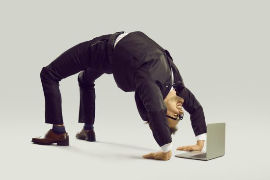 Happy flexible businessman in suit doing yoga while working on his laptop computer
